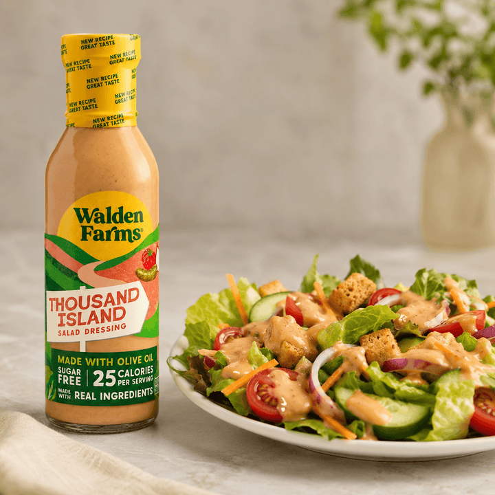 Walden Farms Thousand Island Salad Dressing made with olive oil beside a fresh garden salad topped with tomatoes, cucumbers, onions, croutons, and creamy dressing.