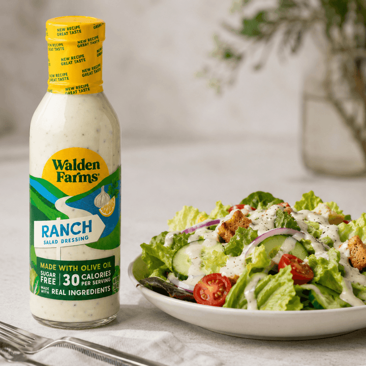 Walden Farms Ranch Salad Dressing made with olive oil beside a crisp garden salad topped with cucumbers, tomatoes, onions, croutons, and creamy ranch dressing.