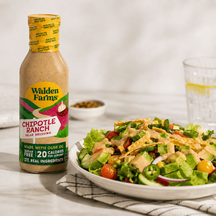 Walden Farms Chipotle Ranch Salad Dressing made with olive oil beside a Southwest-style salad with lettuce, tomatoes, cucumbers, avocado, tortilla strips, jalapeños, and creamy dressing.
