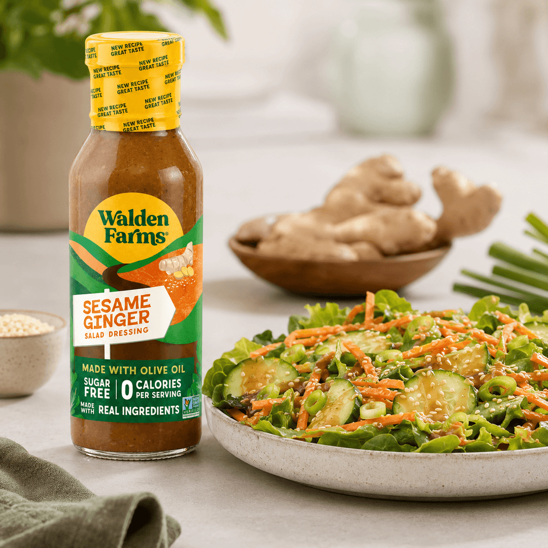 Walden Farms Sesame Ginger Salad Dressing made with olive oil beside an Asian-inspired salad with cucumbers, carrots, sesame seeds, scallions, and ginger dressing.
